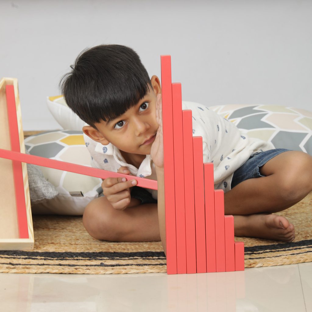 A kid is playing with red rods in montessori kit